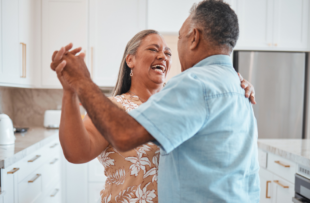 Happy senior couple, dance and laughing in kitchen at home.