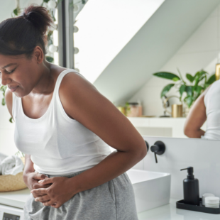 Young woman standing in the bathroom and feeling pain in the stomach area.