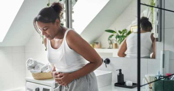 Young woman standing in the bathroom and feeling pain in the stomach area.