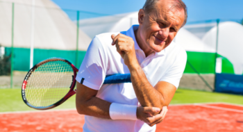 Senior man with elbow pain standing during tennis match on sunny day