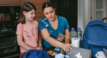 Mother preparing emergency backpack with her daughter in the kitchen