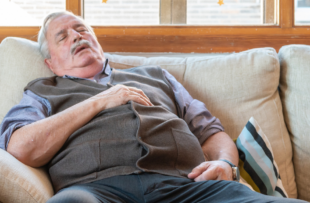 A tired elderly male fall asleep on a comfortable couch in the living room