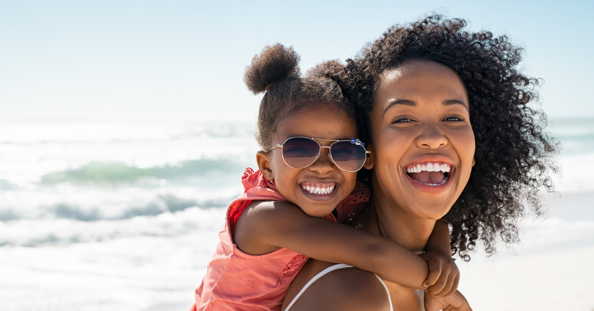 Smiling mother and beautiful daughter wearing sunglasses having fun on the beach.