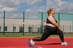 A woman does stretching and squatting on a sports field in an outdoor stadium on a hot summer morning.