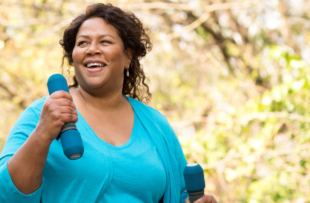 A woman walking in a park with two light dumbbells.