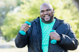 A man walking in a park with two light dumbbells.