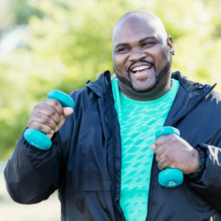 A man walking in a park with two light dumbbells.