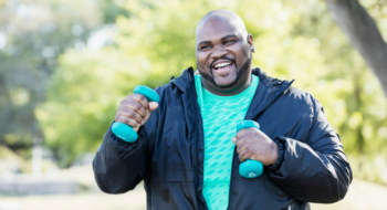 A man walking in a park with two light dumbbells.