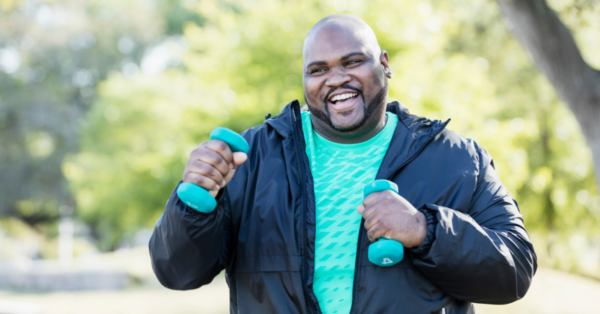 A man walking in a park with two light dumbbells.