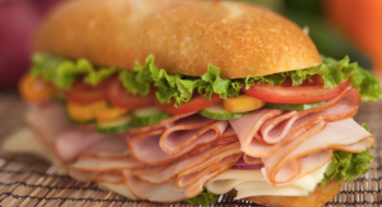 Large sandwich with cheese, deli meats and vegetables on a bamboo place mat