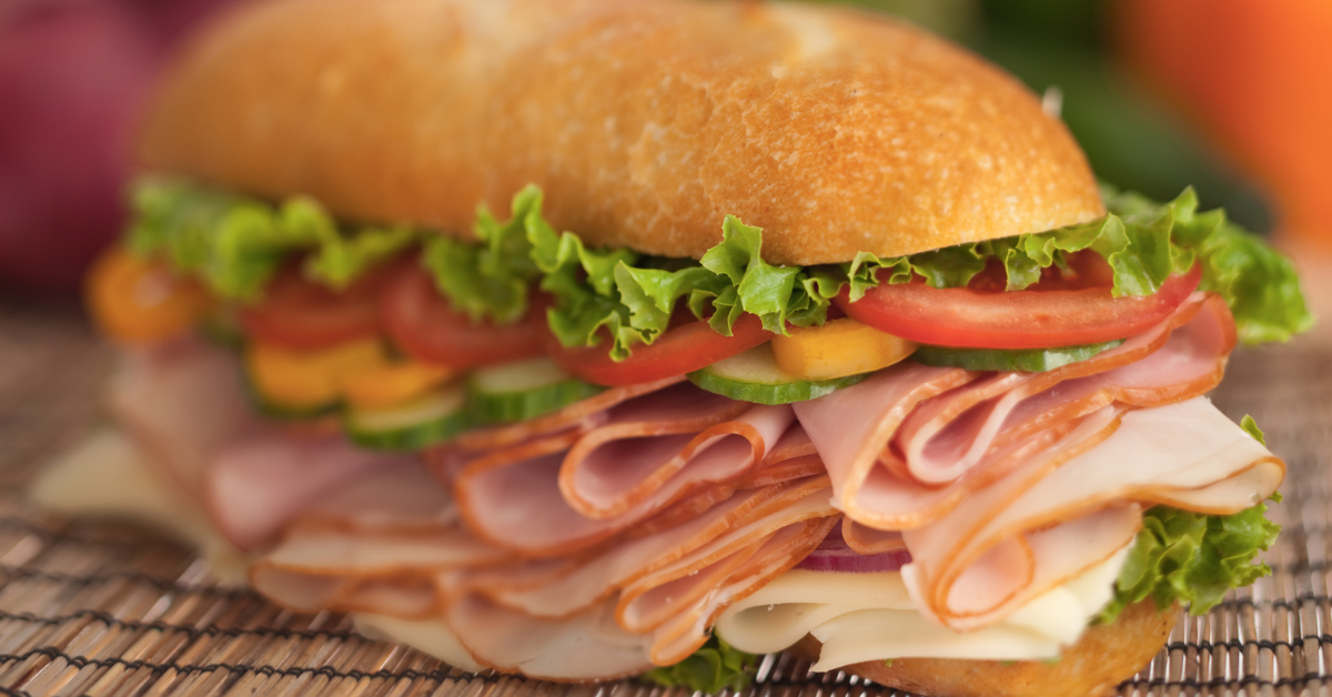 Large sandwich with cheese, deli meats and vegetables on a bamboo place mat