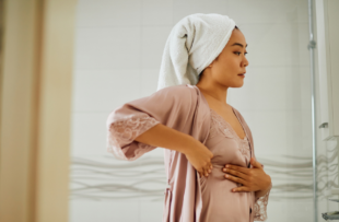 Young woman standing in front of bathroom mirror while doing breast self-examination.