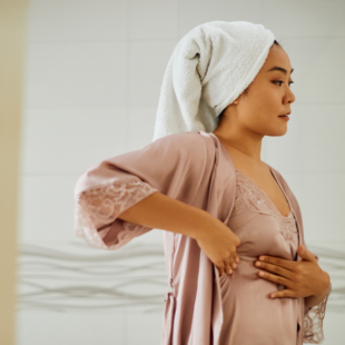 Young woman standing in front of bathroom mirror while doing breast self-examination.