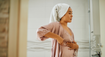 Young woman standing in front of bathroom mirror while doing breast self-examination.