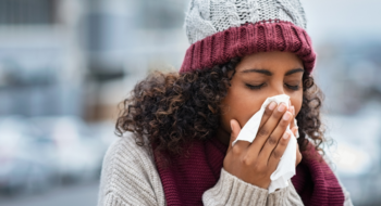 A woman wearing a winter hat and blowing her nose.