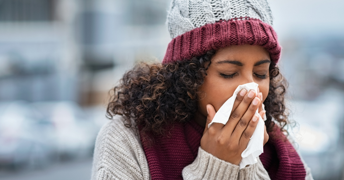 A woman wearing a winter hat and blowing her nose.