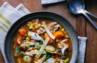 A bowl of chicken tortilla soup on a ktichen table, rested on a tea towel.