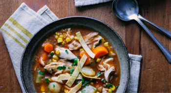 A bowl of chicken tortilla soup on a ktichen table, rested on a tea towel.