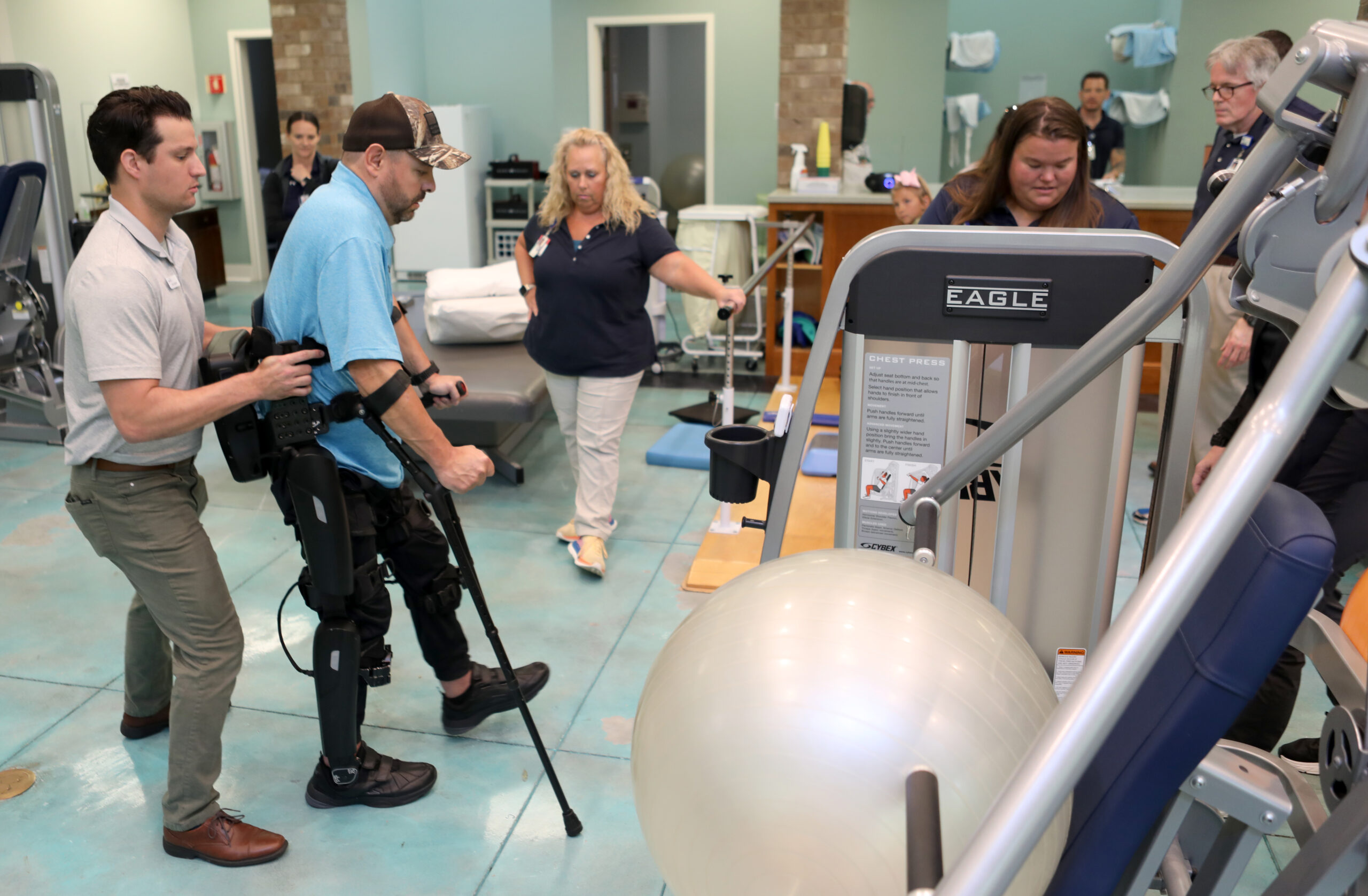 Matt Stewart takes first step in exoskeleton surrounded by his team of therapists. 