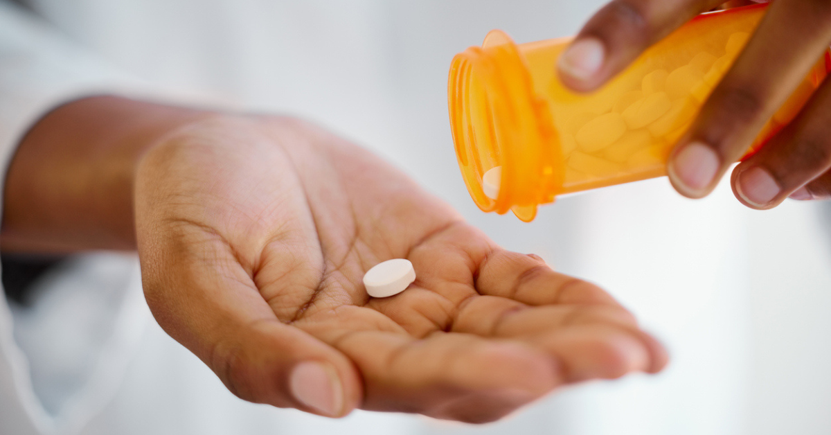 A person holding a pill in their hand and a pill bottle in their other hand, about to pour more into their hand.