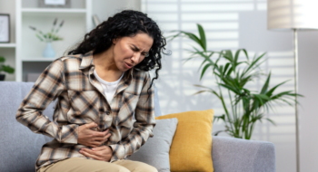 A woman with stomach pain, grabbing her stomach while sitting on the couch.