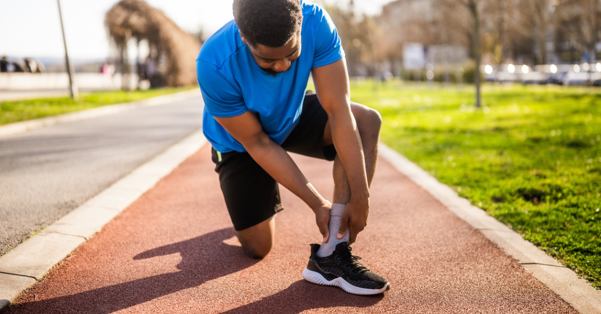 A runner grabbing his ankle on a track path.