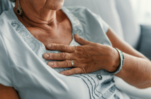 A woman wearing a blue shirt holds her chest in pain.