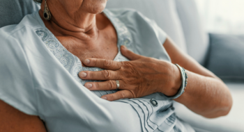 A woman wearing a blue shirt holds her chest in pain.