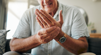 Hands, pain and arthritis with a senior man holding his hand while suffering from osteoporosis, cramp or injury.