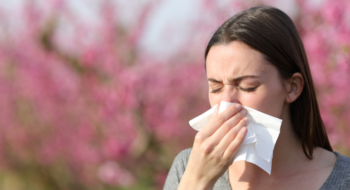 Woman blowing on tissue suffering allergy in spring in a field