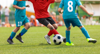 Junior competition between players running and kicking soccer. ball. Anonymous youth junior athletes in red and blue soccer shirts